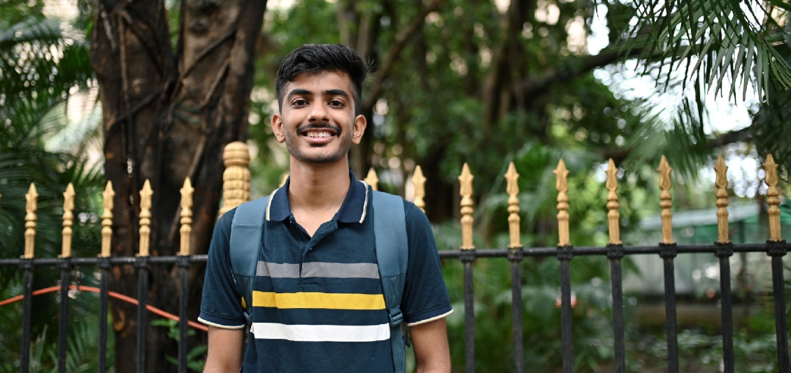 College-aged man with light beard and backpack smiles confidently at the camera